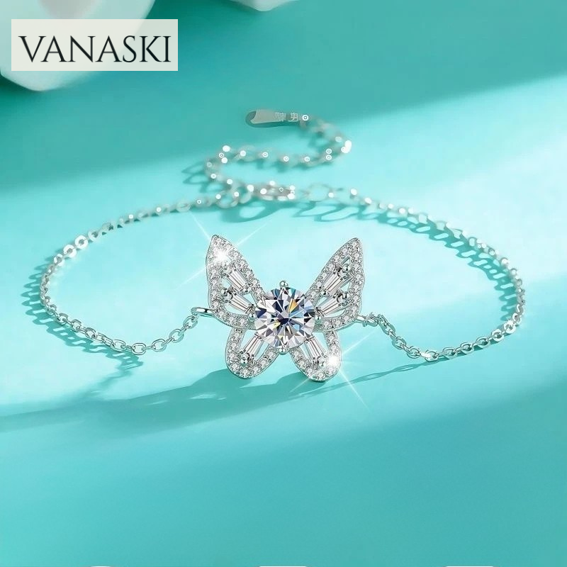 Butterfly-shaped necklace with gemstone on a turquoise background, featuring the brand 'VANASKI'.