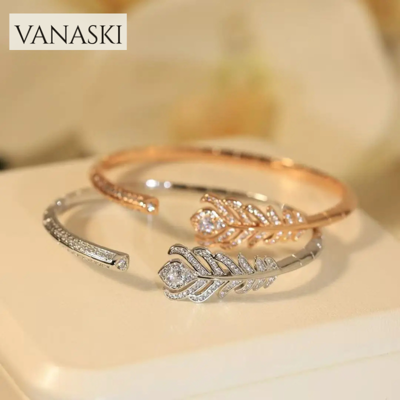 Two feather-shaped bracelets, one rose gold and one silver, on a light background with 'VANASKI' branding.