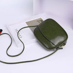 Green leather crossbody bag on a white surface with a book underneath