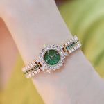 Luxury watch with green face and diamond-like stones on a wrist against a blurred background
