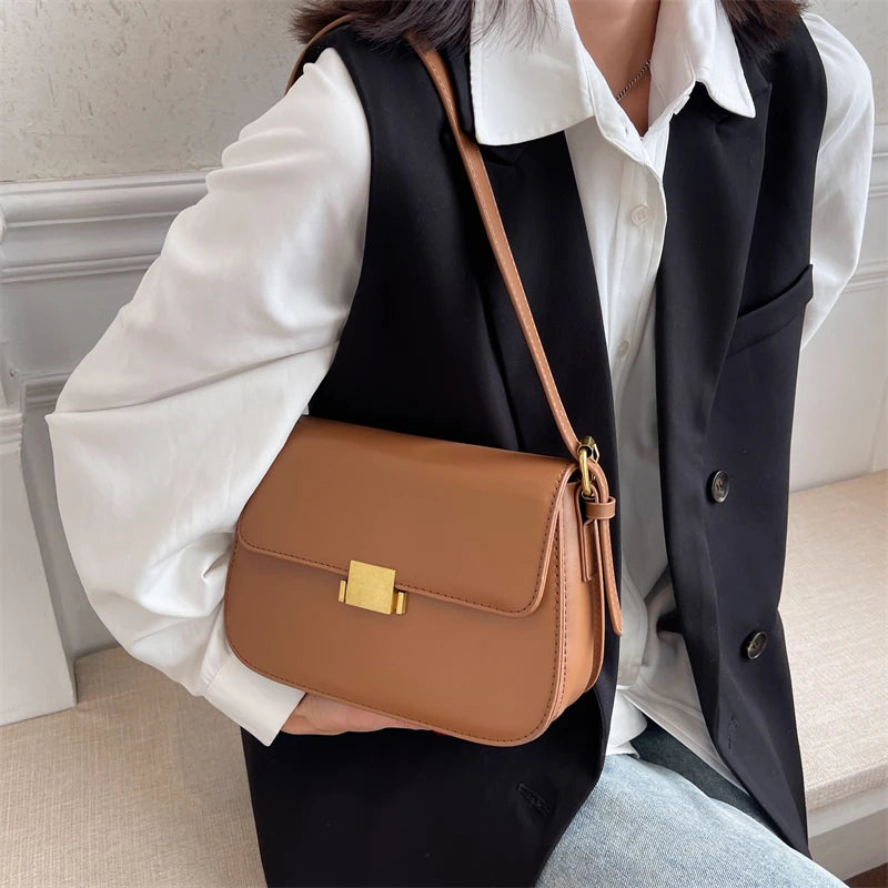 Person holding a brown leather handbag with a gold clasp indoors.