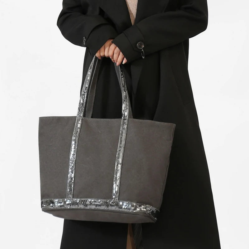 Person holding a gray tote bag with silver sequin trim against a white background