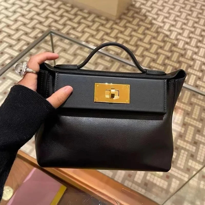 Black handbag with gold clasp held by a person on a patterned floor.