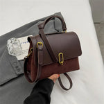 Brown leather handbag with gold accents held by a hand on a neutral background