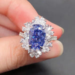 Blue gemstone ring with diamond accents held between fingers against a dark background