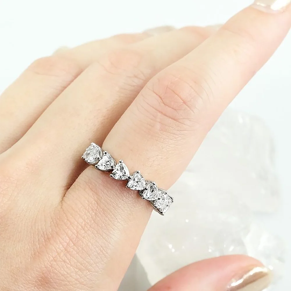 Silver ring with heart-shaped gemstones on a hand against a white background