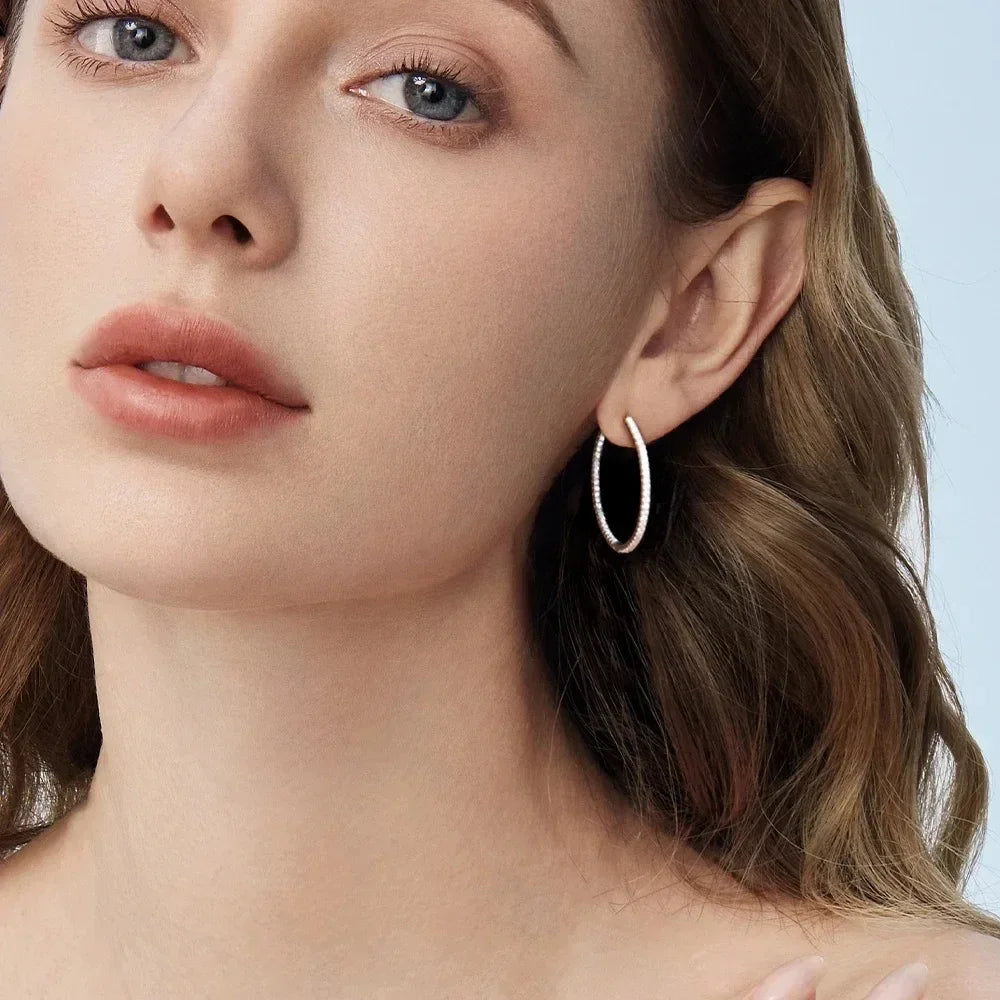 Close-up of a woman wearing gold hoop earrings with a light blue background