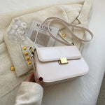White handbag with gold accents held by a hand on a textured surface