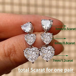 Heart-shaped diamond earrings held between fingers with size labels on a blurred background