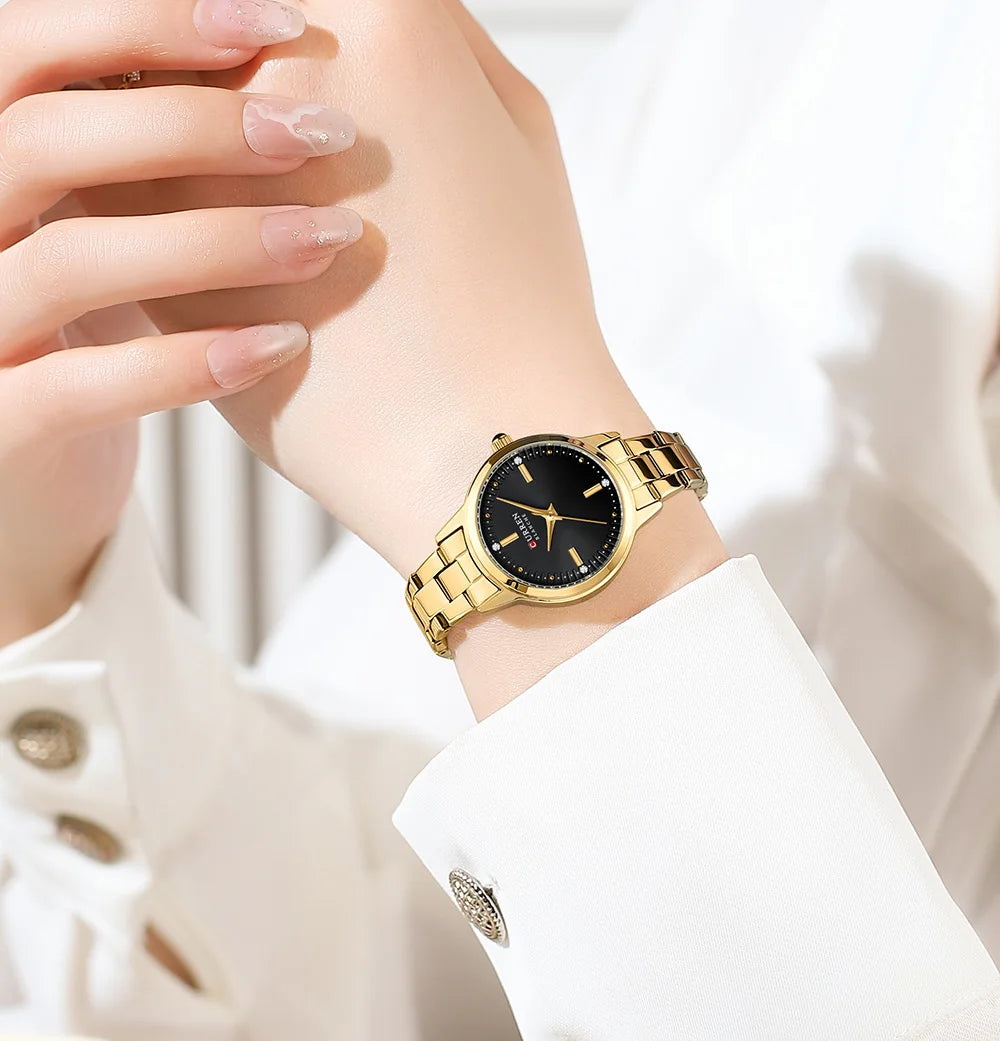 Gold wristwatch with black dial on a person's wrist against a white background
