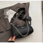 Black handbag with gold chain detail on a gray coat with a glass and book.