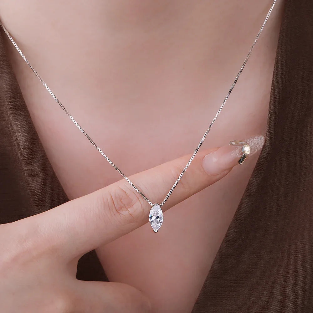 Silver necklace with a clear pendant held by a hand against a brown background