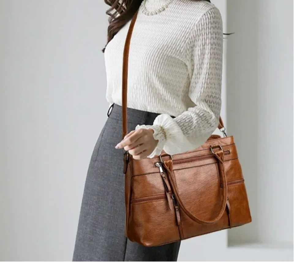 Person holding a brown leather handbag against a plain background