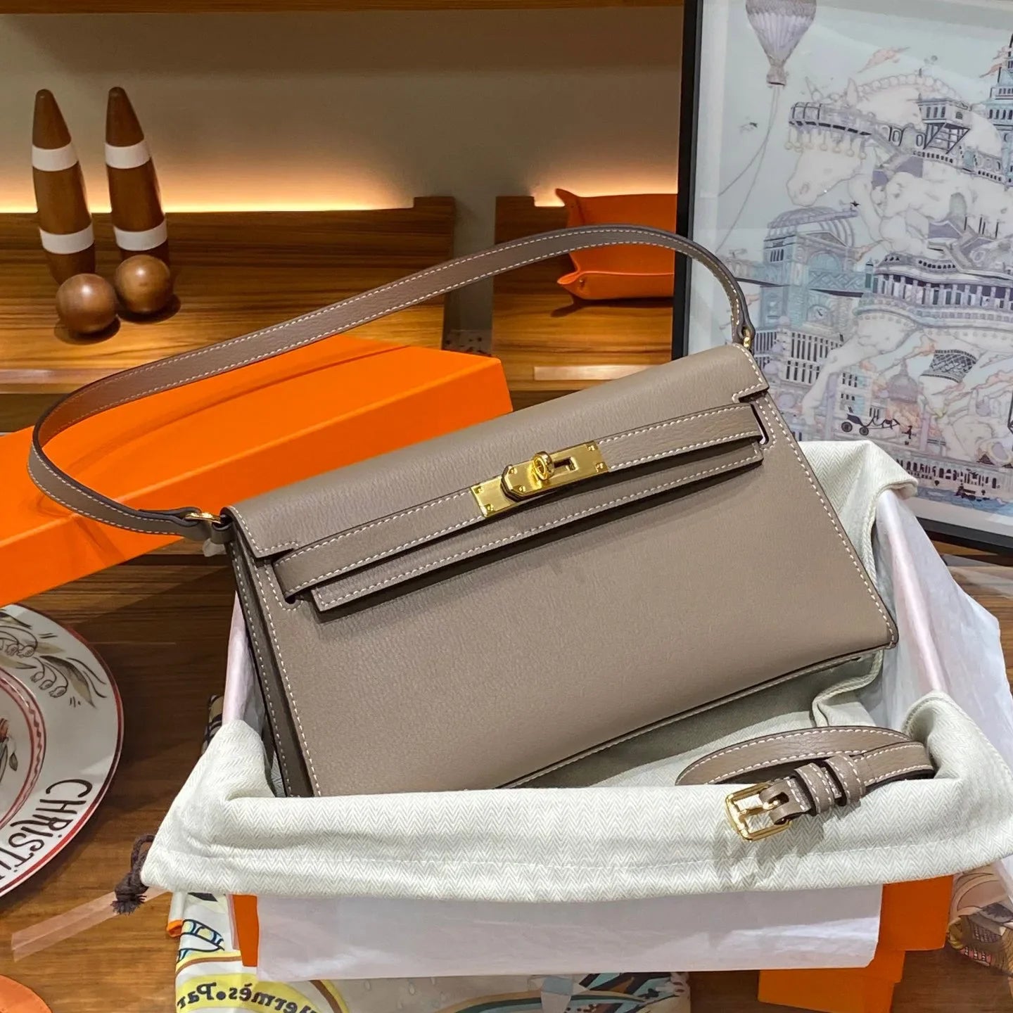 Beige handbag with gold hardware on a wooden surface with decorative items.