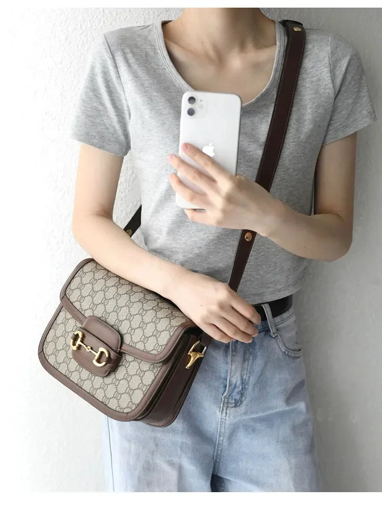Person holding a phone with a Gucci handbag over their shoulder against a plain background
