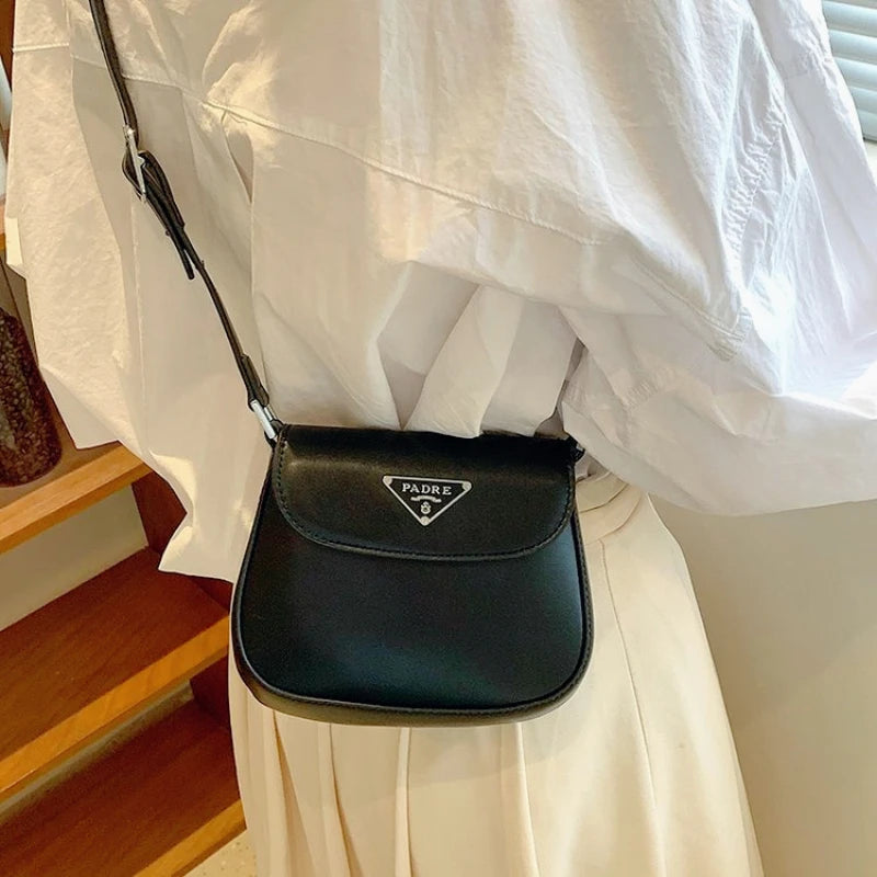 Person wearing a black Prada handbag with a white shirt and beige pants.