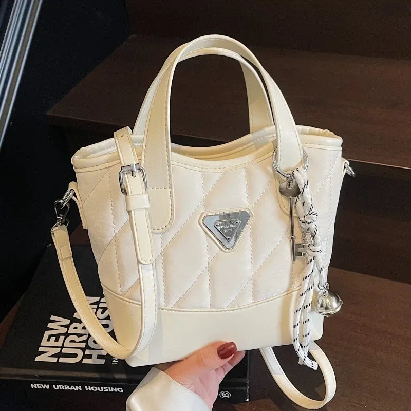 White quilted handbag with a brand logo held by a hand on a dark surface.