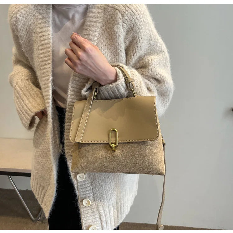 Beige handbag held by a person wearing a beige cardigan against a neutral background