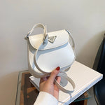 White handbag with a Prada logo held by a hand on a glass table.