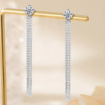 Pair of silver earrings with chain details on a gold stand against a beige background