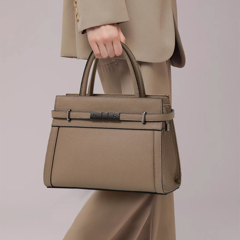 Person holding a beige handbag with a matching suit against a neutral background