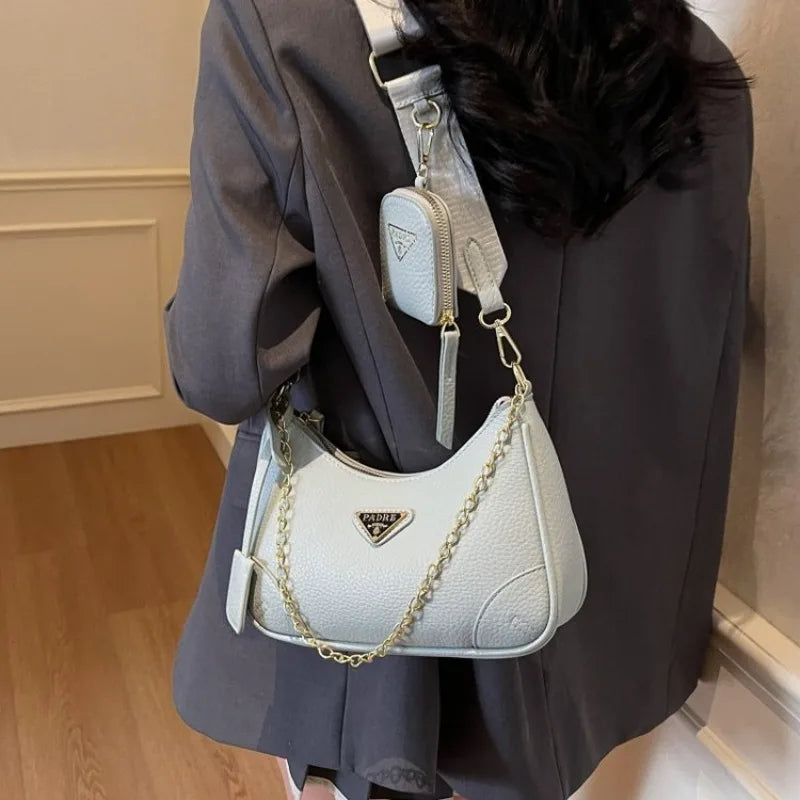 White handbag with gold chain detail worn by a person in a dark coat.