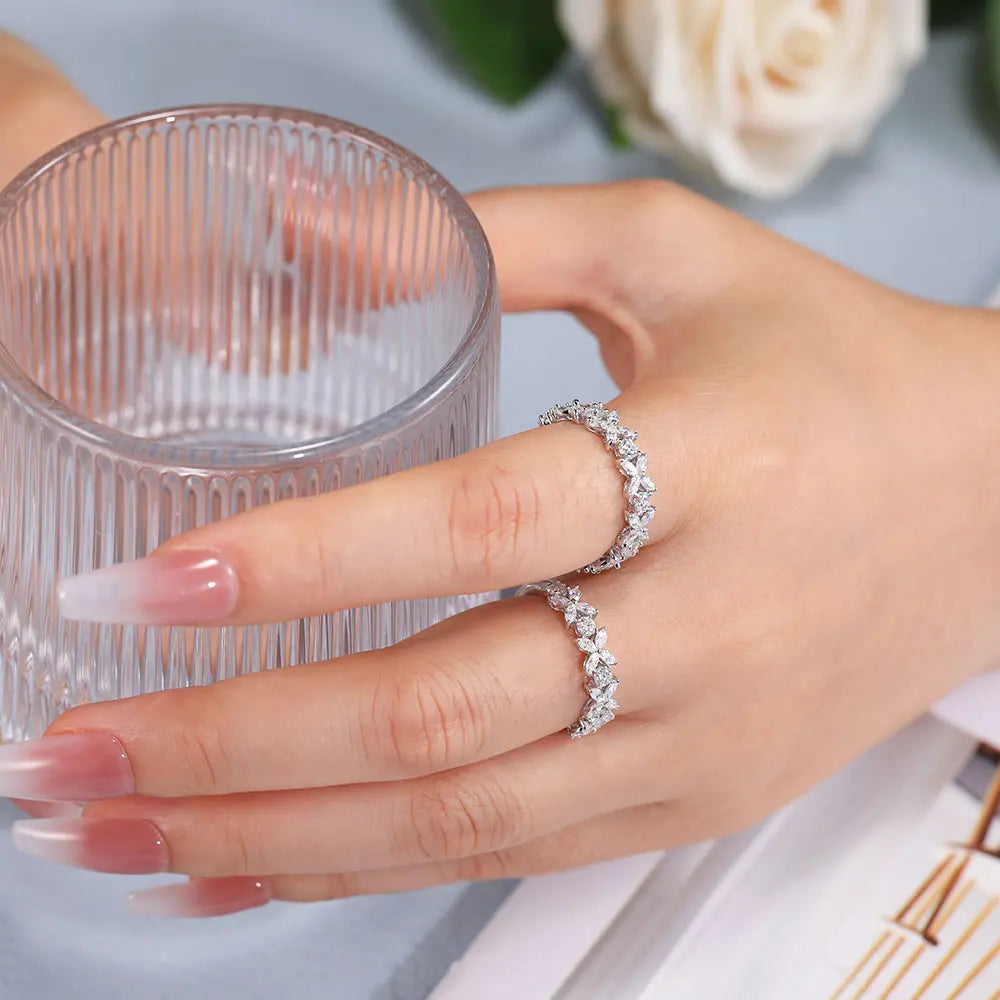 Hand wearing a diamond ring holding a clear glass with white roses in the background