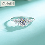 Silver ring with a large central gemstone and smaller stones on a light blue background, featuring the brand 'VANASKI'.