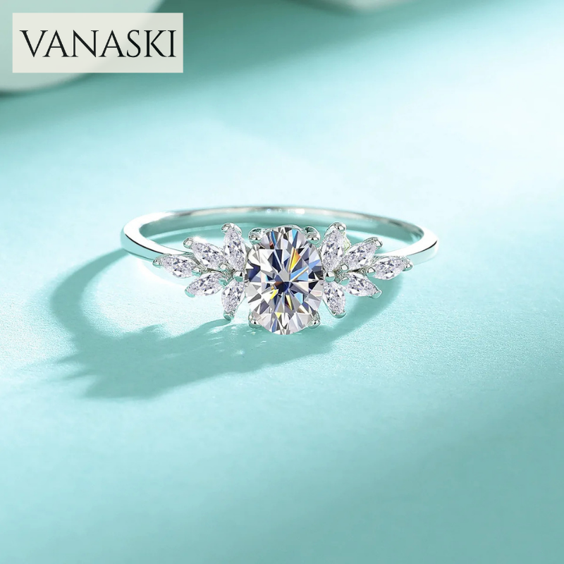 Silver ring with a large central gemstone and smaller stones on a light blue background, featuring the brand 'VANASKI'.