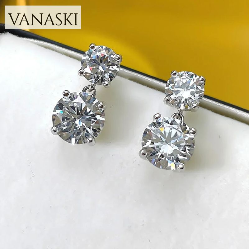 Pair of diamond earrings on a white surface with 'VANASKI' branding.