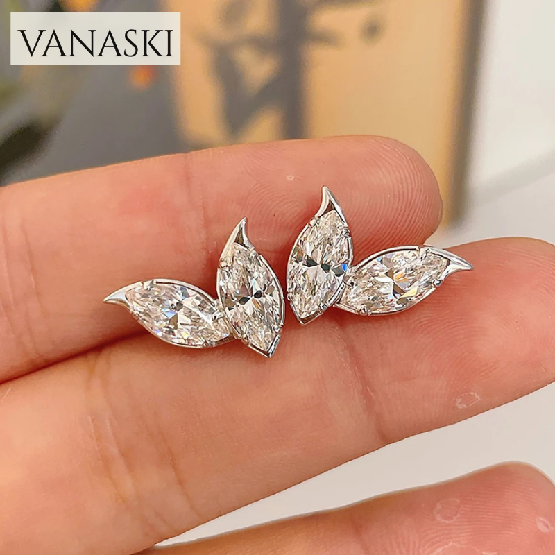 Silver leaf-shaped earrings held between fingers with 'VANASKI' branding above.