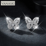 Butterfly-shaped earrings with sparkling stones on a dark background, featuring the VANASKI brand.