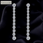 Pair of silver earrings with clear stones on a dark fabric background, branded 'VANASKI'.