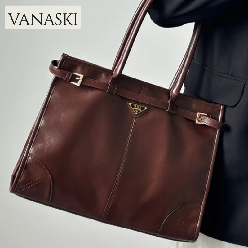 Brown leather handbag held by a person wearing a dark coat, with 'VANASKI' branding.