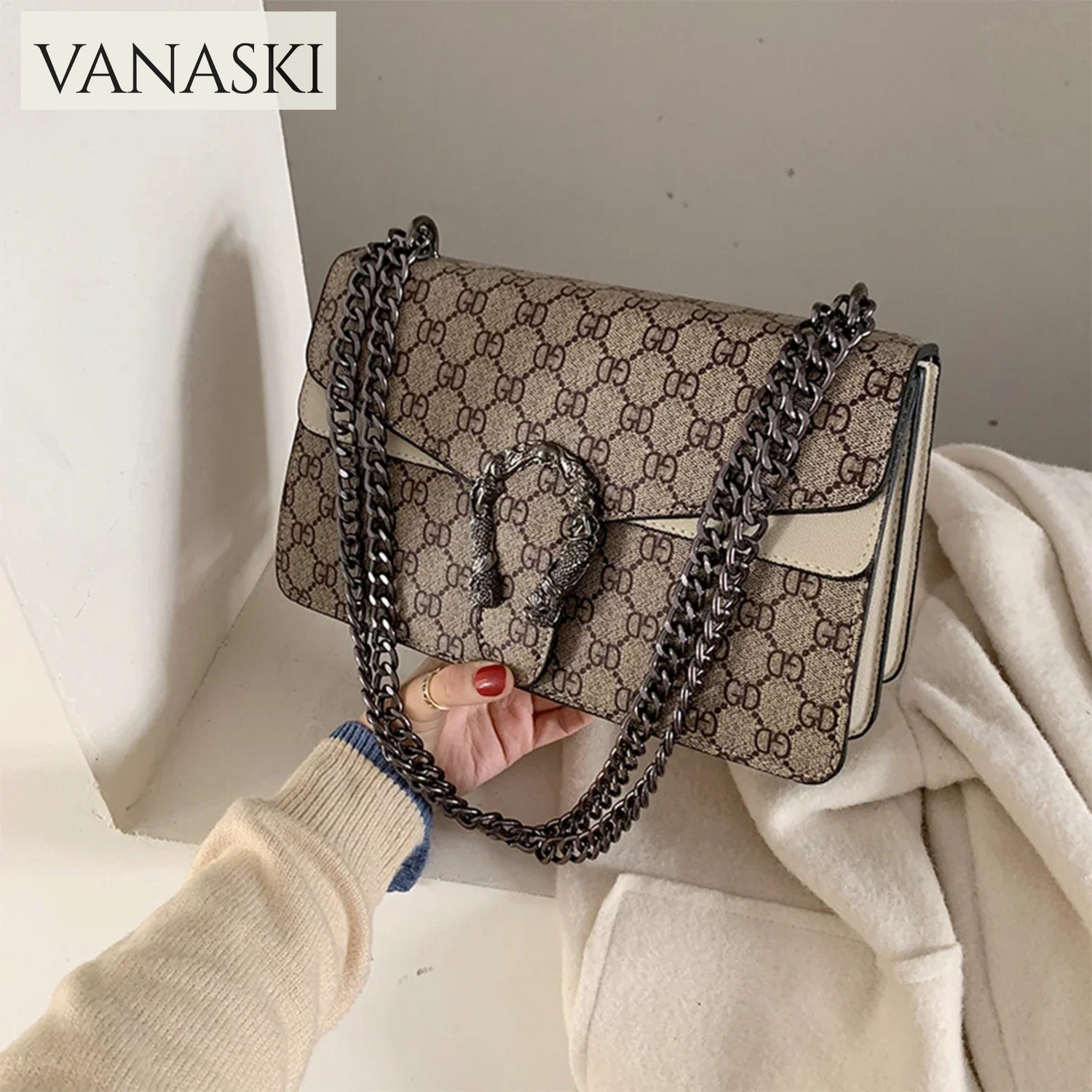Patterned handbag with chain detail held by a person wearing a beige sweater.