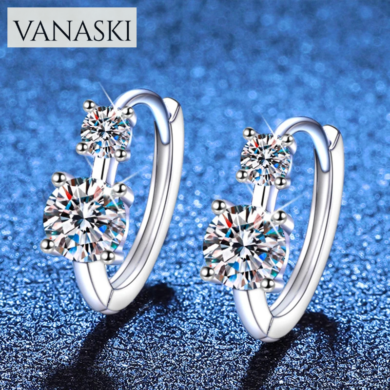 Silver hoop earrings with clear gemstones on a blue glittery background, featuring the Vanaski brand.