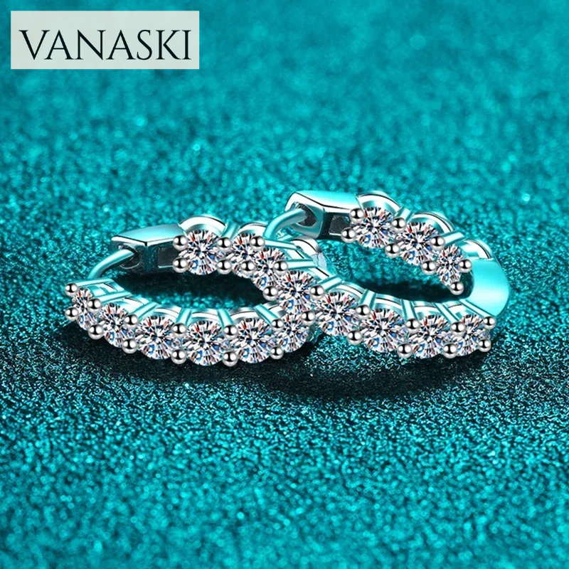 Pair of silver hoop earrings with clear stones on a teal background, featuring the Vanaski brand.