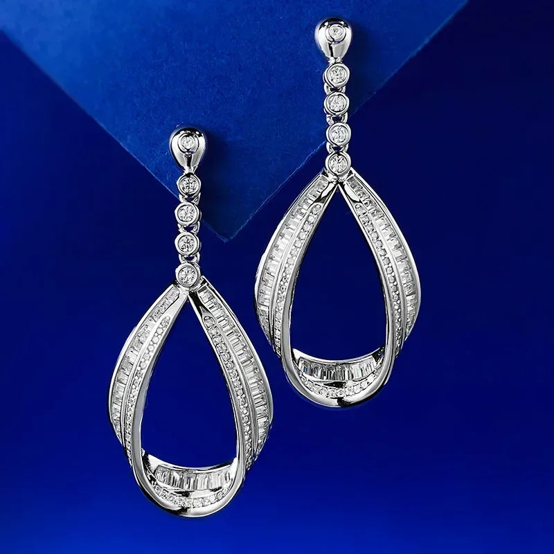 Pair of silver teardrop earrings with clear stones on a blue background