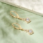 Gold earrings with clear gemstones on a light green fabric background