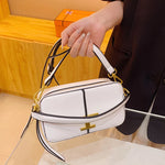 White handbag with gold accents held by a person against a wooden background