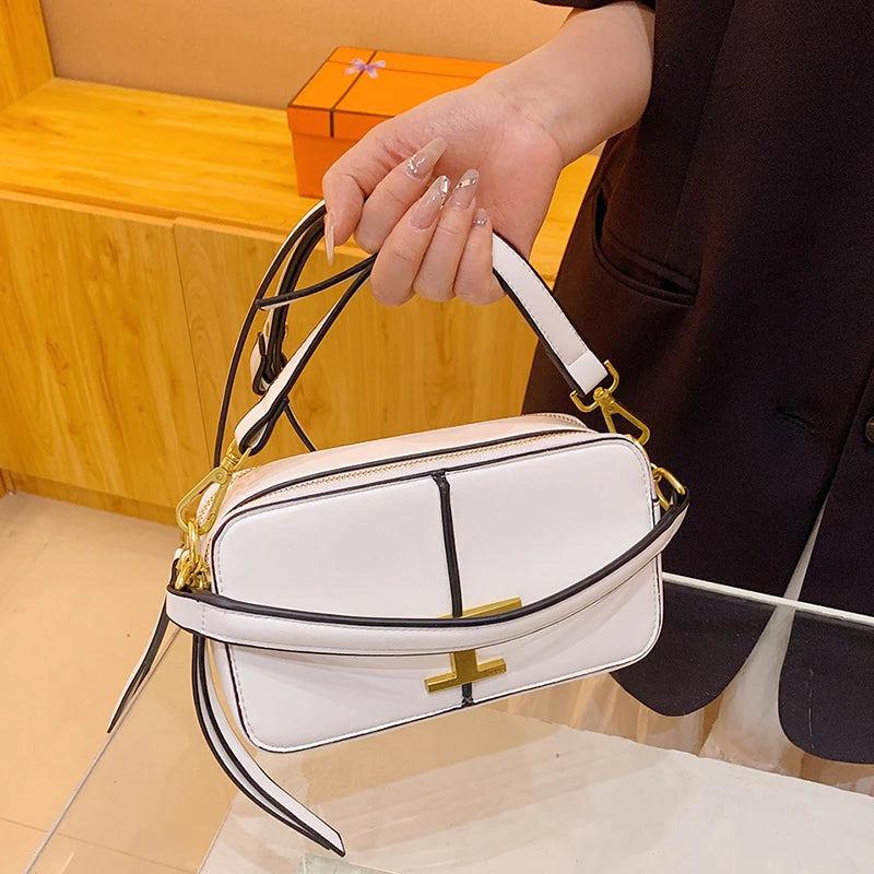 White handbag with gold accents held by a person against a wooden background