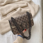Patterned handbag with chain strap held by a hand against a soft fabric background
