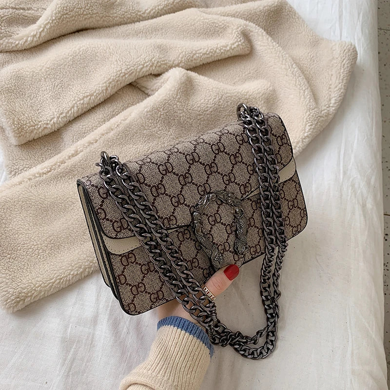 Patterned handbag with chain strap held by a hand against a soft fabric background