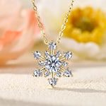 Snowflake-shaped diamond pendant on a gold chain with a blurred floral background