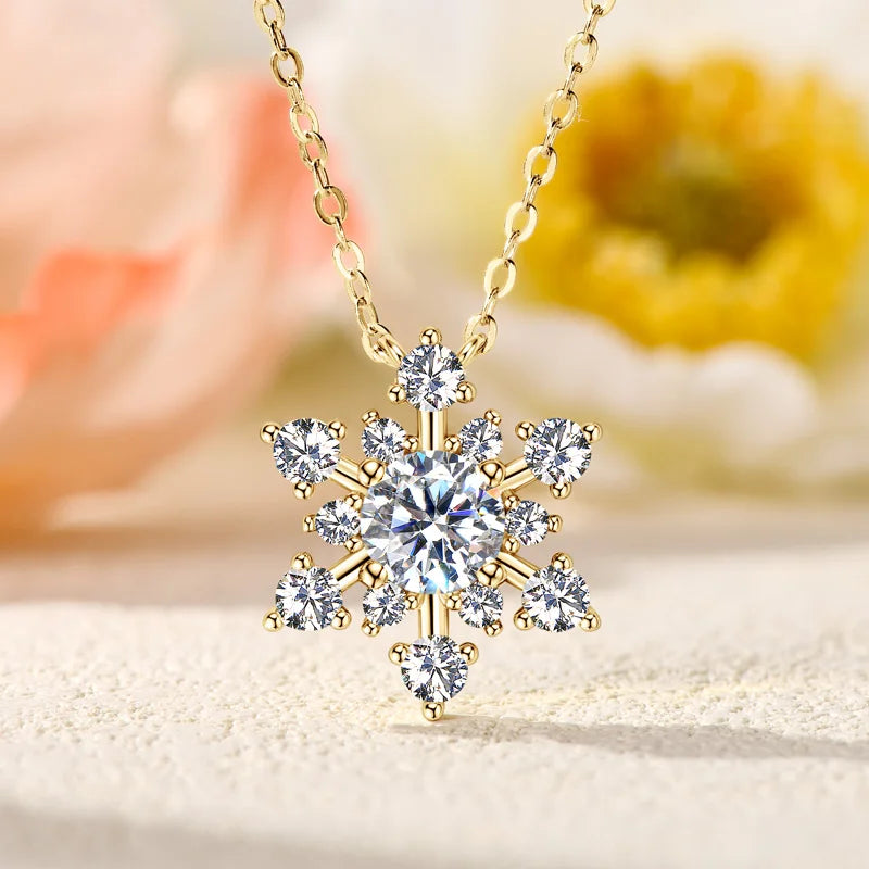 Snowflake-shaped diamond pendant on a gold chain with a blurred floral background