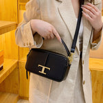 Person holding a black handbag with a gold 'T' logo in front of a wooden background