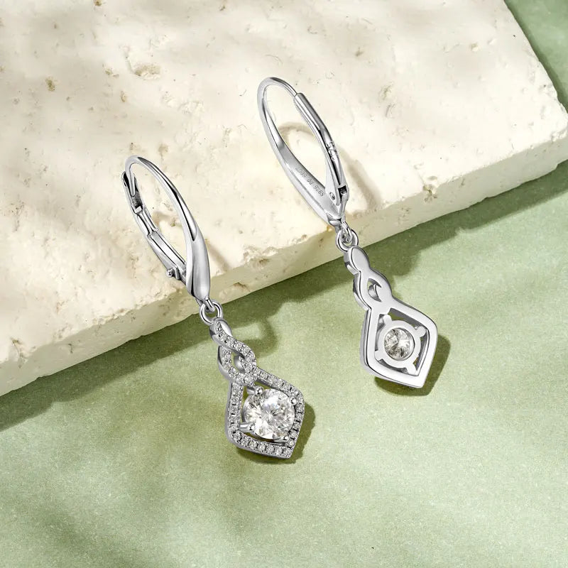 Silver earrings with gemstones on a light stone and green fabric background