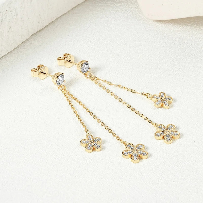 Gold earrings with chain and clover designs on a white background