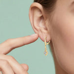 Gold earring being worn on an ear with a green background