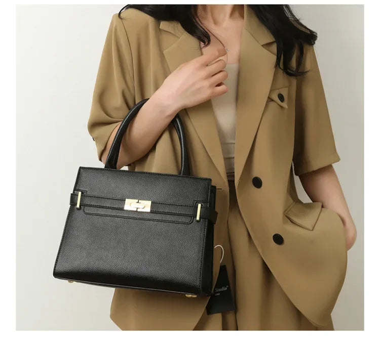 Person wearing a beige coat holding a black handbag against a plain background